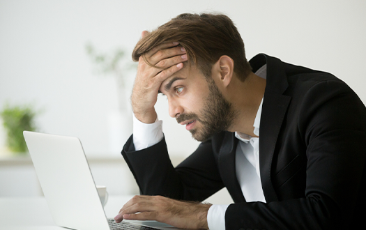 A man wearing a suit looks at his laptop realizing he made a mistake. 